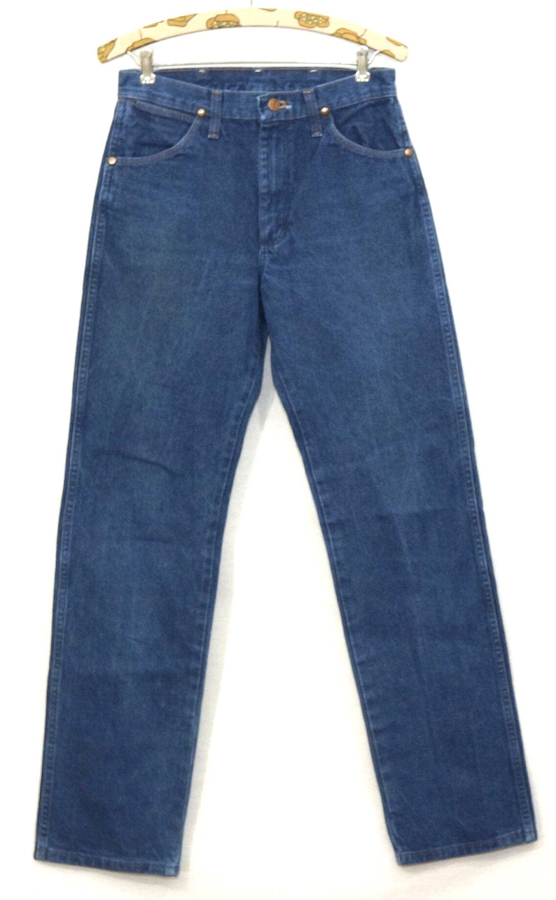 May include: Blue denim jeans with a classic five-pocket design. The jeans are hung on a vintage patterned hanger. The jeans have a straight leg cut and a button and zipper closure. The denim has a medium wash.