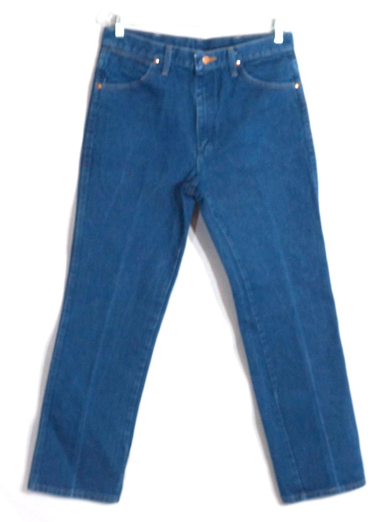 May include: A pair of blue denim jeans with a classic five-pocket design. The jeans have a straight leg cut and are hanging against a white background. The jeans have a button and zip closure, and copper-coloured rivets.