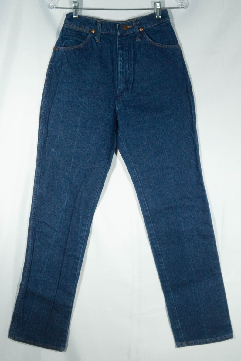 May include: Dark blue denim jeans with a high waist and straight leg. The jeans have classic five-pocket styling, copper rivets, and a button and zipper closure. The garment is hanging on a clear hanger against a white background.