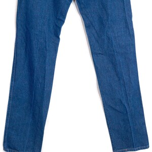 May include: A pair of classic blue denim jeans. The jeans have a straight leg cut and a medium wash. The image shows the jeans from the waist down, with the legs slightly spread apart. The fabric appears to be a sturdy cotton denim.
