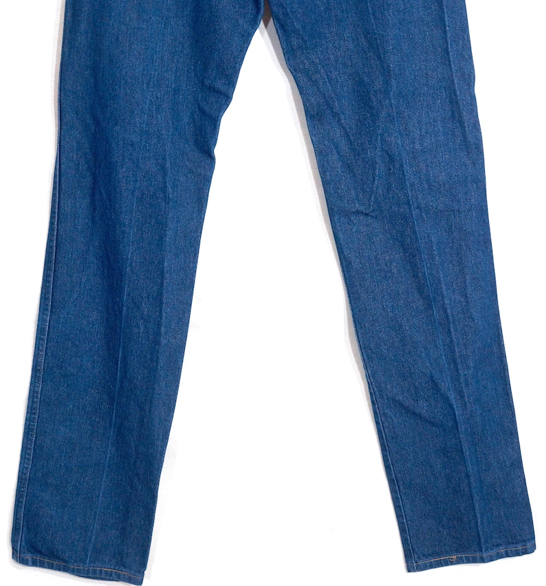 May include: A pair of classic blue denim jeans. The jeans have a straight leg cut and a medium wash. The image shows the jeans from the waist down, with the legs slightly spread apart. The fabric appears to be a sturdy cotton denim.