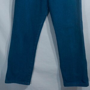 May include: A pair of blue jeans. The jeans are a medium wash denim with a straight leg cut. The image shows the lower portion of the jeans, from the upper thighs to the ankles. The background is a plain white.