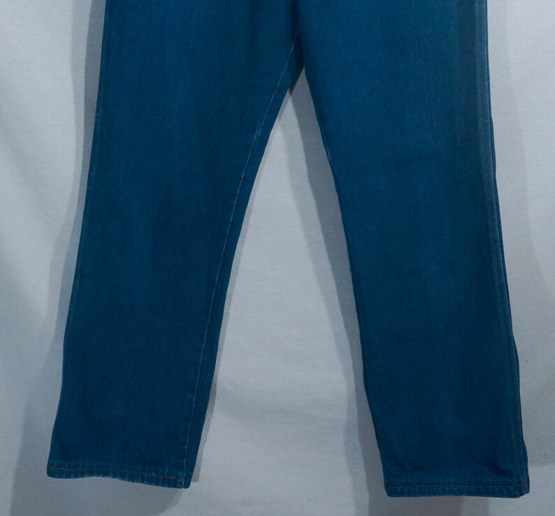 May include: A pair of blue jeans. The jeans are a medium wash denim with a straight leg cut. The image shows the lower portion of the jeans, from the upper thighs to the ankles. The background is a plain white.