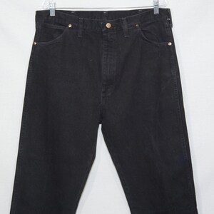May include: Black denim jeans with a classic five-pocket design. The jeans have a button and zipper closure, and brass rivets. The jeans are hanging on a white background.