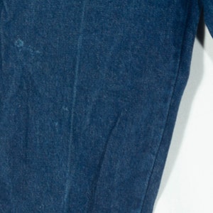 May include: Close-up of dark blue denim jeans. The image shows the texture and stitching details of the fabric. The jeans appear to be new or in excellent condition, with no visible wear and tear.