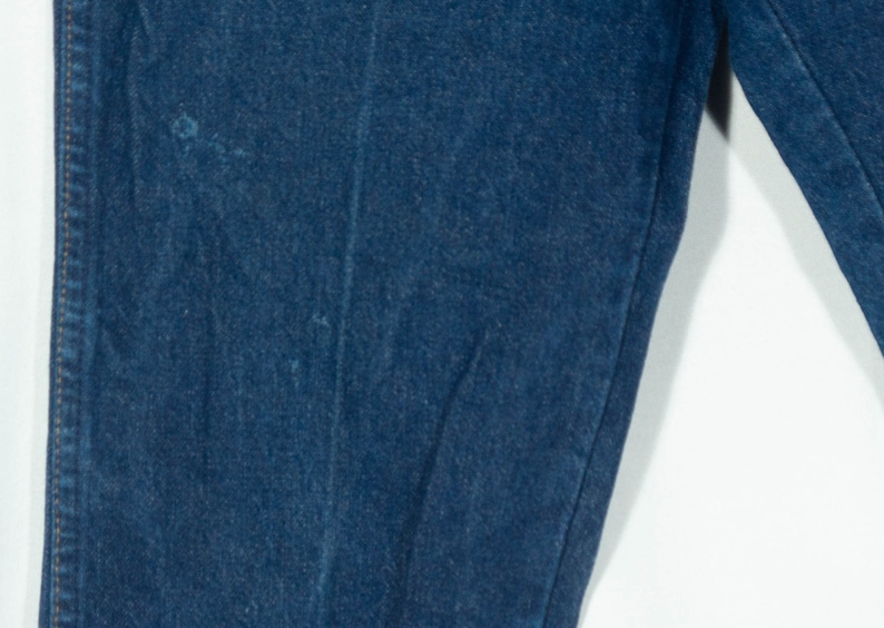 May include: Close-up of dark blue denim jeans. The image shows the texture and stitching details of the fabric. The jeans appear to be new or in excellent condition, with no visible wear and tear.