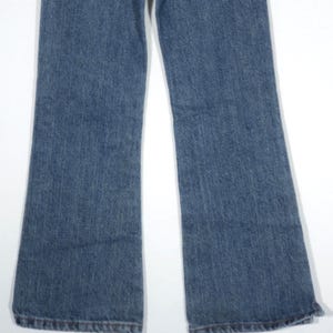 May include: A pair of blue denim jeans with a flared leg design. The jeans have a classic five-pocket style and a medium wash. The hem of the jeans is finished with a traditional stitch.