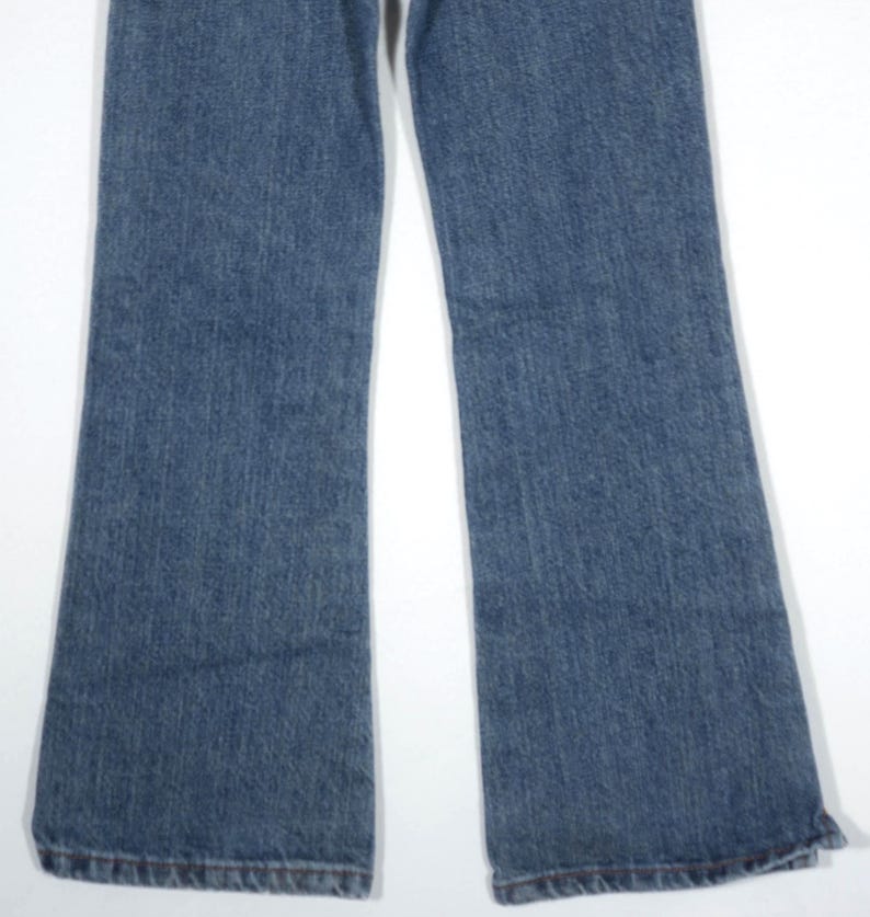 May include: A pair of blue denim jeans with a flared leg design. The jeans have a classic five-pocket style and a medium wash. The hem of the jeans is finished with a traditional stitch.