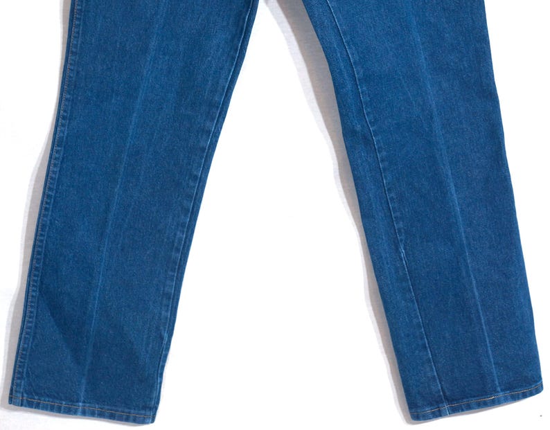 May include: Close-up of blue denim jeans. The jeans have a classic straight-leg cut and feature a visible seam down the front of each leg. The denim has a medium wash and a slightly faded appearance.