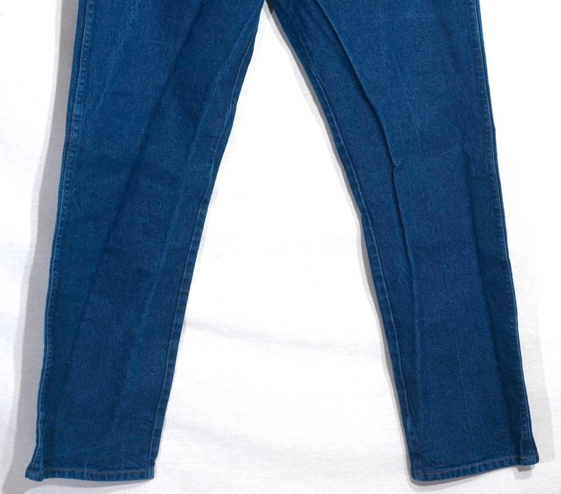 May include: Close-up of blue denim jeans. The jeans have a classic straight-leg cut and are made of a medium-wash denim fabric. The image shows the front of the jeans, with the legs slightly spread apart.