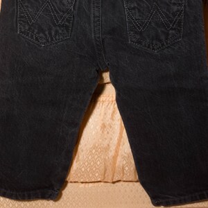 May include: Close-up of black denim shorts. The shorts feature two back pockets with a stitched design. The denim has a slightly faded appearance. The shorts are a classic style, suitable for casual wear.