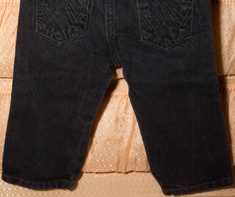 May include: Close-up of black denim shorts. The shorts feature two back pockets with a stitched design. The denim has a slightly faded appearance. The shorts are a classic style, suitable for casual wear.