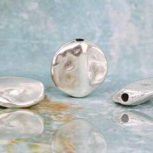May include: Three silver metal beads with a hole through the center. The beads are irregularly shaped and have a smooth, shiny finish.