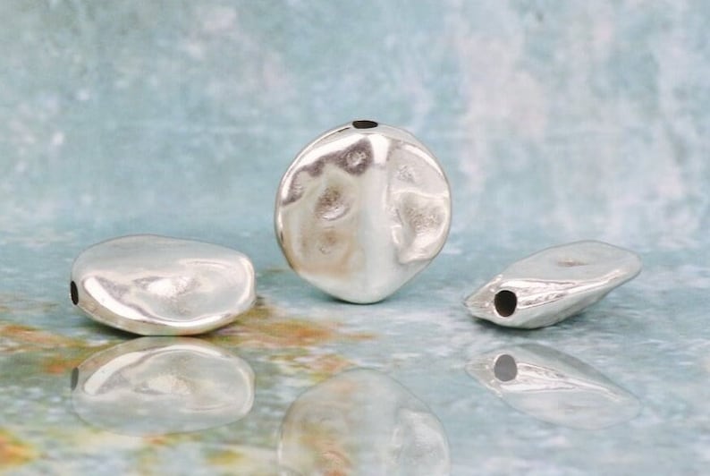 May include: Three silver metal beads with a hole through the center. The beads are irregularly shaped and have a smooth, shiny finish.