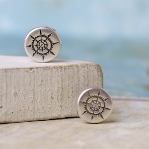 May include: Two silver metal beads with a circular design featuring a sunburst pattern. The beads are on a white surface.
