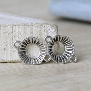May include: Two silver-toned metal connector charms with a decorative, textured, circular design. Each charm has two jump rings for attaching to jewellery.