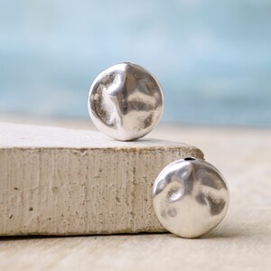 May include: Two silver-toned metal beads with a hammered texture and a hole through the center.