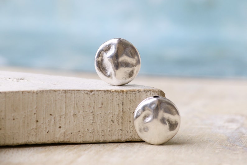 May include: Two silver-toned metal beads with a hammered texture and a hole through the center.