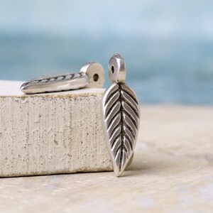 May include: Two silver leaf-shaped charms with a textured design. The charms have a hole at the top for attaching to jewelry or other crafts.