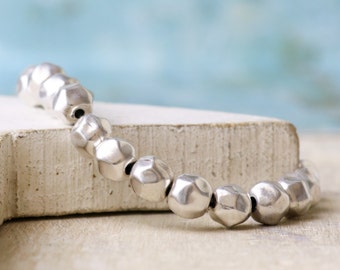 Könnte beinhalten: Ein silbernes Armband mit facettierten Perlen. Die Perlen sind rund und haben eine gehämmerte Textur. Das Armband liegt auf einer weißen Oberfläche.