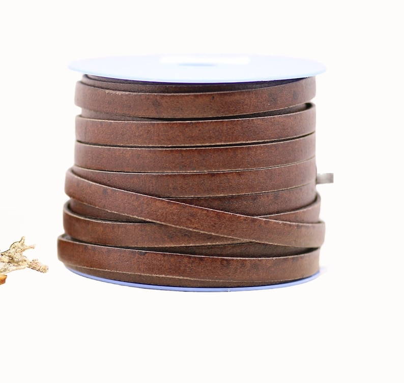 May include: A spool of brown leather cord, wound around a blue plastic bobbin. The cord is approximately 5 mm wide.