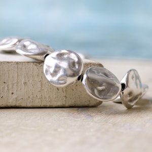 May include: A silver bracelet with a hammered metal design. The bracelet is made up of several round, flat pieces of metal that are connected together.