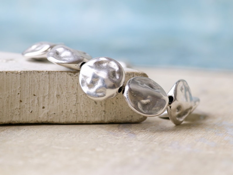 May include: A silver bracelet with a hammered metal design. The bracelet is made up of several round, flat pieces of metal that are connected together.