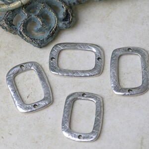 Pu&ograve; includere: Quattro ciondoli rettangolari in metallo argentato con superficie testurizzata e due fori su ogni lato.