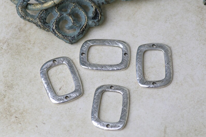 Pu&ograve; includere: Quattro ciondoli rettangolari in metallo argentato con superficie testurizzata e due fori su ogni lato.