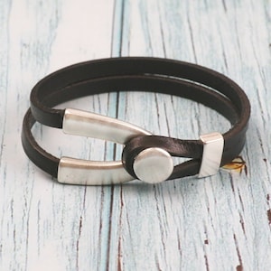 May include: A black leather bracelet with a silver metal clasp. The bracelet is double-layered and has a simple design.