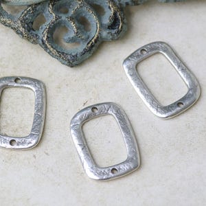 Pu&ograve; includere: Tre ciondoli rettangolari in metallo argentato con superficie testurizzata e due fori nella parte superiore.