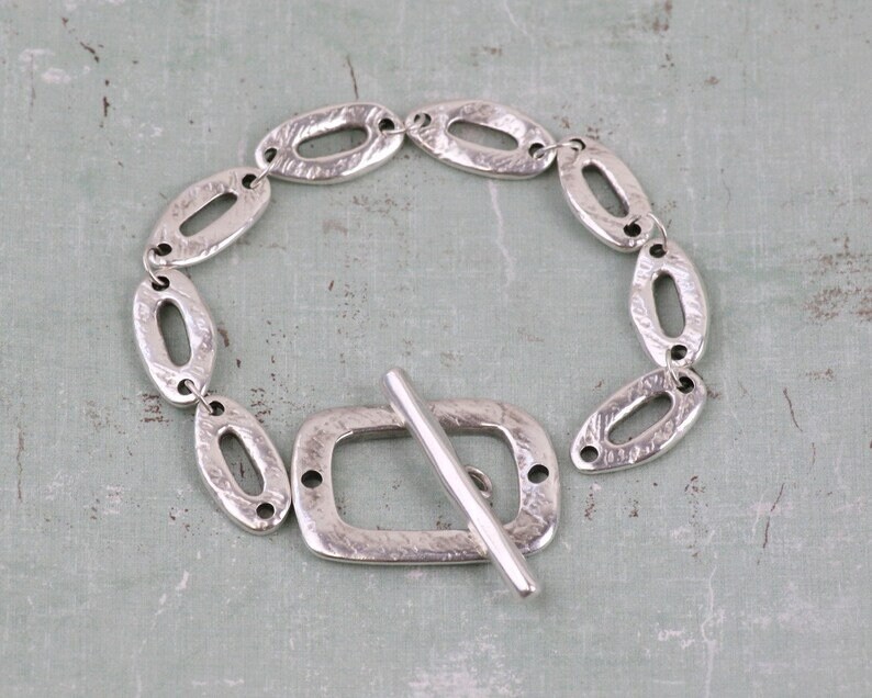 Pu&ograve; includere: Un braccialetto d'argento con una catena a maglie ovali testurizzate e una chiusura a scorrimento quadrata.