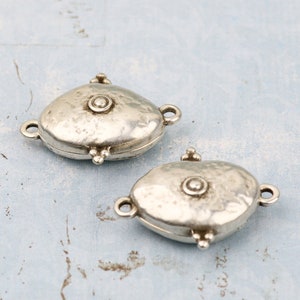 May include: Two silver oval-shaped clasps with a textured surface and a small round bead in the center. The clasps have a hinged design and are perfect for adding a unique touch to jewelry.