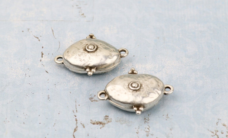 May include: Two silver oval-shaped clasps with a textured surface and a small round bead in the center. The clasps have a hinged design and are perfect for adding a unique touch to jewelry.
