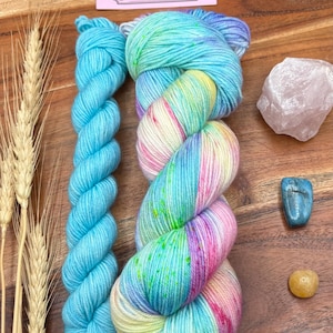 May include: A close-up of hand-dyed yarn in shades of blue, pink, and yellow, with a solid blue skein. The image includes a rose quartz crystal, a blue gemstone, and a yellow gemstone. The text on the card reads "Potions and Purls - Hand Dyed Yarn."