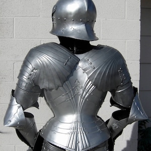 May include: A detailed view of a medieval suit of armor, showcasing a polished, silver-colored helmet and body armor. The armor features intricate designs and rivets, reflecting light. The image highlights the back of the armor, emphasizing its historical craftsmanship.