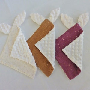 May include: Three baby burp cloths with white, brown, and purple fabric. Each cloth has a white, textured side and a patterned side with gold glitter. The cloths have bunny ear shapes at the top.
