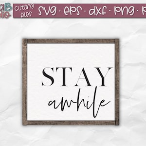 May include: A white sign with a wood frame, featuring the text "STAY awhile" in black lettering. The text "STAY" is in a bold, sans-serif font, while "awhile" is in a cursive script font.