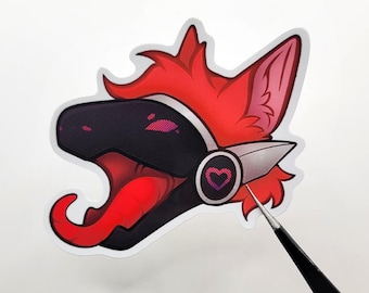 May include: A die-cut sticker featuring a stylized creature head with bright red fur, a black visor, and a long red tongue. The character wears a silver headset with a pink pixelated heart icon on the side, rendered in a vibrant digital art style.