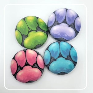 May include: Four circular buttons featuring a stylized paw pad design. Each button displays a different color scheme: one lime green, one lavender purple, one bright pink, and one cyan blue. The paw pads are outlined in dark gray.