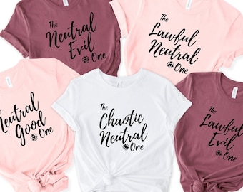 May include: Five t-shirts with different alignment charts printed on them. The shirts are in pink, white, and maroon. The text on the shirts reads "The Neutral Evil One", "The Lawful Neutral One", "The Neutral Good One", "The Chaotic Neutral One", and "The Lawful Evil One".