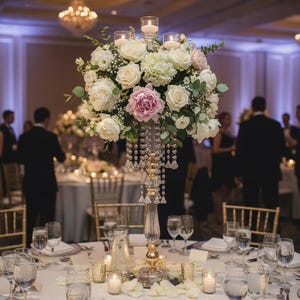 Puede incluir: Un centro de mesa alto de oro y cristal transparente que sostiene un gran arreglo floral de rosas blancas, hortensias y una peon&iacute;a rosa, acentuado con cuentas de cristal colgantes y tres peque&ntilde;os portavelas de vidrio.
