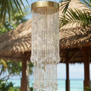 May include: A cylindrical hanging light fixture featuring a gold-toned metal frame and multiple tiers of clear, faceted crystal beads. The structure is suspended by a thin metal chain, with the crystal strands cascading downward in a layered design.