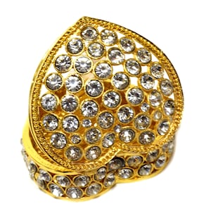 Puede incluir: Una caja de corazón de oro con un diseño de cristal transparente. La caja está cerrada y los cristales son visibles.