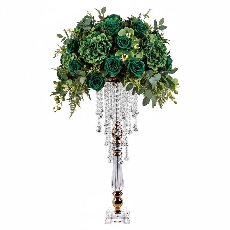 Puede incluir: Un centro de mesa alto con un arreglo denso de rosas, hortensias y follaje de eucalipto en color verde esmeralda oscuro sobre un soporte de acr&iacute;lico transparente adornado con cuentas de cristal que cuelgan de la base del ramo.