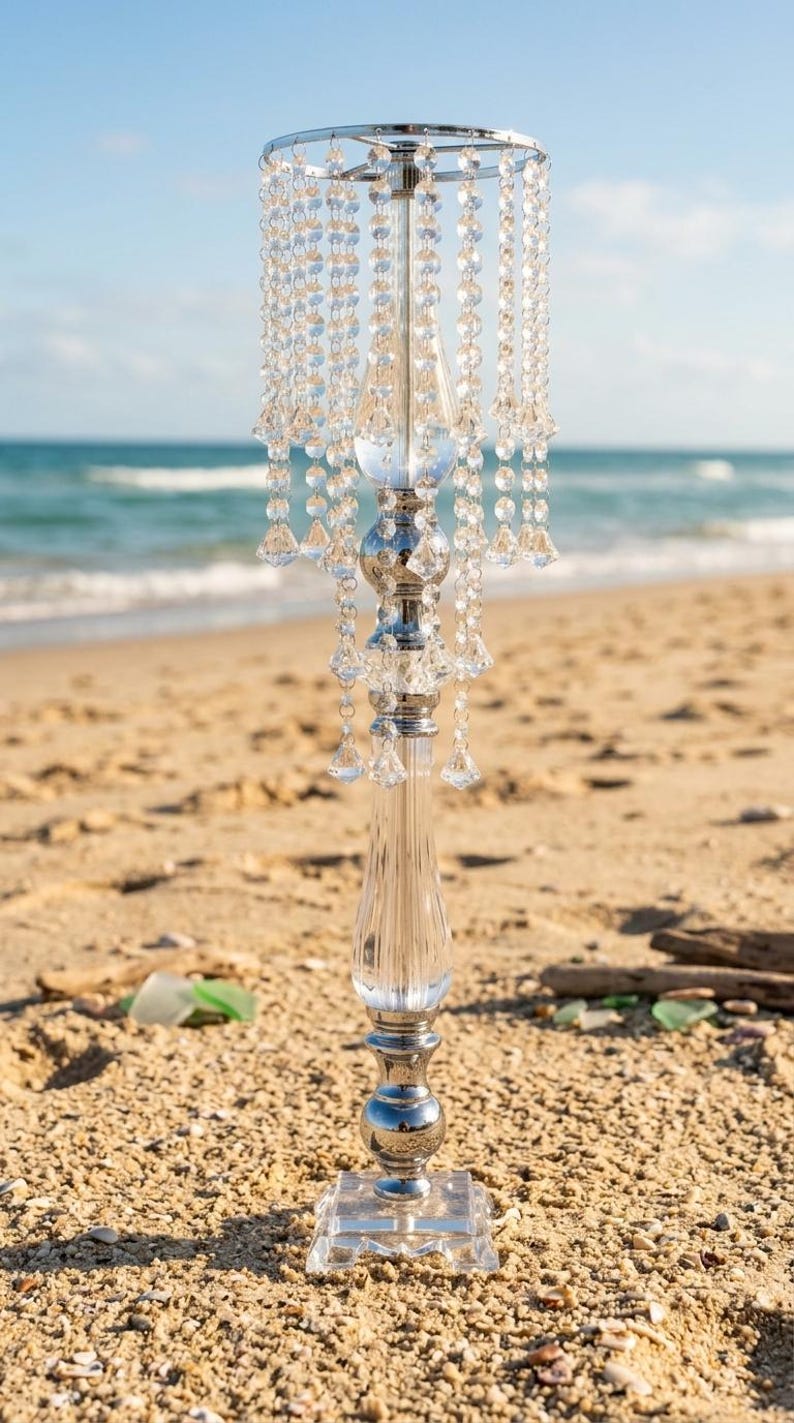 Puede incluir: Un soporte alto para centro de mesa hecho de metal plateado y acr&iacute;lico transparente, con una base cuadrada, una columna central con esferas decorativas y un borde superior circular adornado con m&uacute;ltiples hilos de cuentas transparentes.