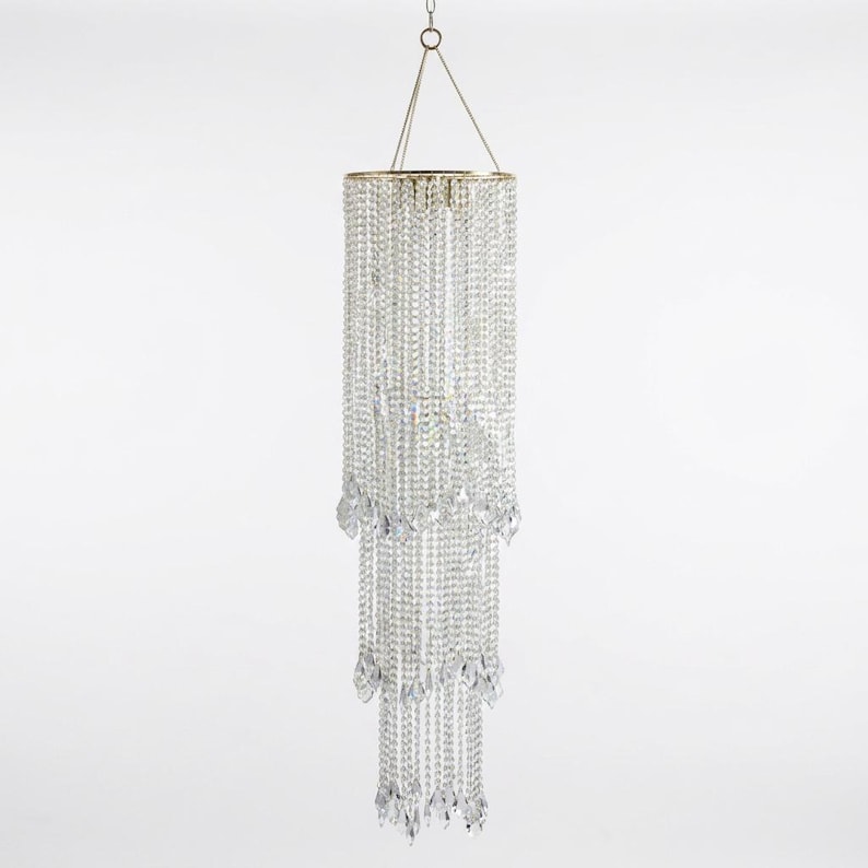 May include: A tiered chandelier featuring multiple strands of clear, faceted crystal beads suspended from a circular gold-toned frame. The fixture is arranged in three distinct levels, with each strand ending in a teardrop-shaped crystal pendant.