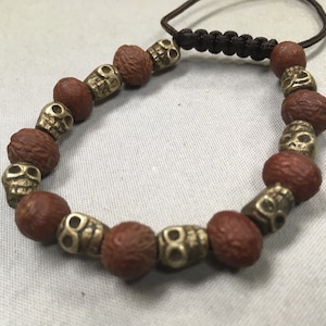 Introducing our stunning Brass Skulls & Raktu Bodhi Seed Mala Bracelet, a perfect addition to any Tibetan boho or tribal style. Each bracele