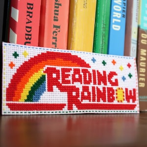 May include: A white cross-stitch bookmark with a rainbow and the text "Reading Rainbow".