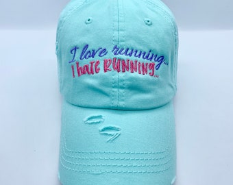 May include: A light blue distressed baseball cap with the embroidered text "I love running... I hate RUNNING..." in pink and purple.